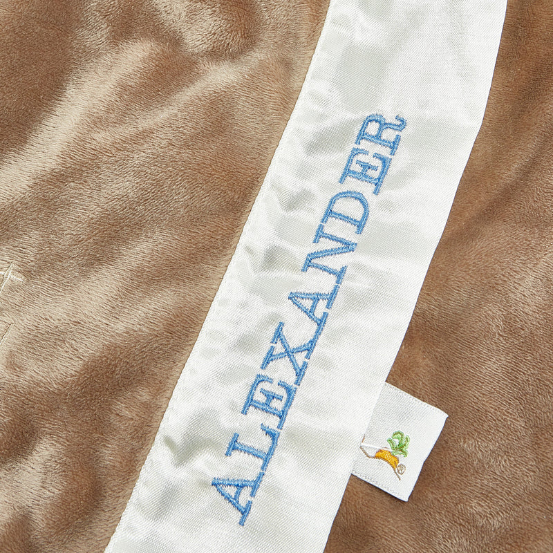Close up image of "Alexander" embroidered in blue on a white and brown blanket 