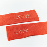 Two orange scarves with embroidered names on a white background