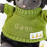 Plush sheep toy wearing a green knitted sweater with 'Owen' embroidered on it.