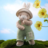 Taupe and white bunny plush in a green outfit with a cream hat.