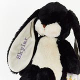 A black and white plush bunny stuffed animal with long floppy ears, one of which is embroidered with the name 'Skylar' in purple. The bunny has a soft cream face and chest, with a small brown stitched nose.