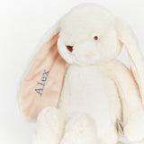 A plush white bunny toy with long floppy ears, one of which is turned inward to show a pale pink lining embroidered with the name 'Alex' in blue. The bunny has small brown embroidered eyes and nose, and a small sewn tag is visible near the bottom right.
