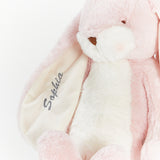 Close-up of a pink plush bunny toy with a white muzzle and inner ear, embroidered name 'Sophia' on the inner ear, on a white background.