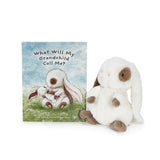 A children's book titled "What Will My Grandchild Call Me?" standing next to a plush stuffed bunny. The bunny is white with brown ears, paws, and feet, and the book cover shows an illustration of a white bunny hugging another in a grassy field under a blue sky.