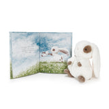 A plush white bunny toy with brown ears, eyes, and paws sits beside an open children's picture book showing a matching bunny illustration on a white background.