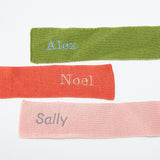 Flat lay of Three scarves in green, red, and pink with embroidered names on a white background