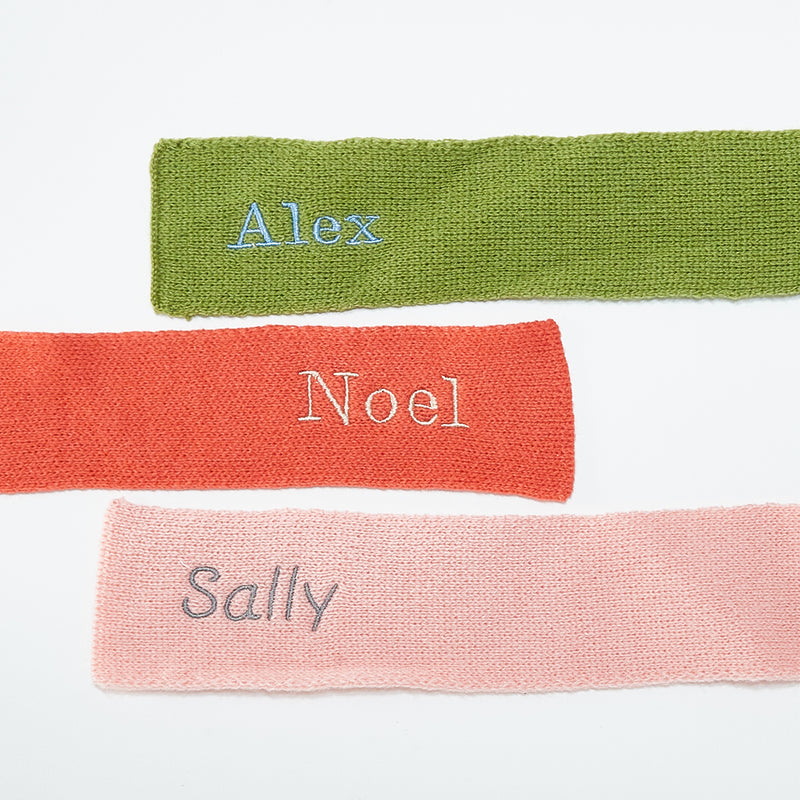 Flat lay of Three scarves in green, red, and pink with embroidered names on a white background