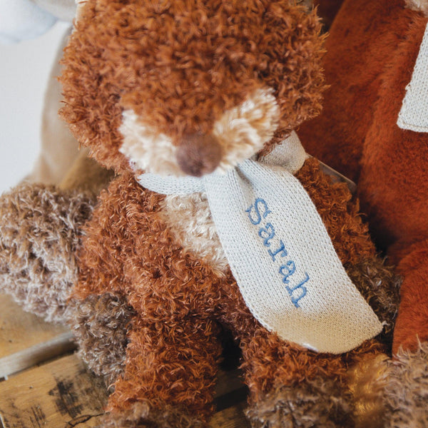 Lifestyle shot of Fox plush with a knit scarf embroidered with 'Sarah' sitting on a wooden surface