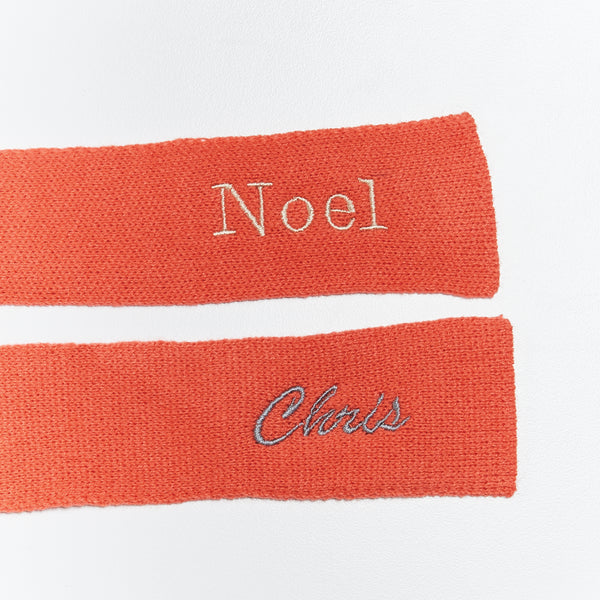 Two red knit scarves with embroidered names on a white background