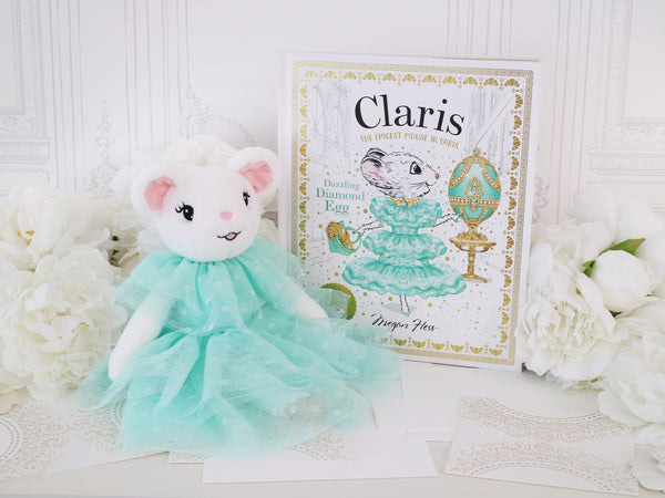 Plush Claris the Mouse toy in a turquoise dress next to a book titled Claris The Mouse - Dazzling Diamond Egg Hardcover Book on a white background with flowers.