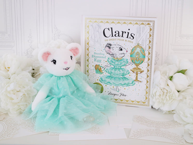 Plush Claris the Mouse toy in a turquoise dress next to a book titled Claris The Mouse - Dazzling Diamond Egg Hardcover Book on a white background with flowers.
