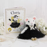 A plush mouse doll dressed in a black tutu with a white bow sits beside its illustrated book labeled 'Claris' on a white surface with decorative flowers and paper props.