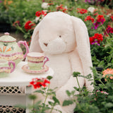 Plush rabbit sitting at a tea set in a garden with flowers in the background