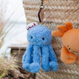 Blue plush octopus keychain with a white hat on a straw bag.