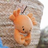 Small orange plush crab bag charm with a tag on a woven surface