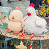 Two plush chickens on a rustic table with a children's book in the background.