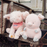 Two pink plush toys resembling pigs sitting on a rustic wooden surface.
