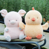 Two plush toys, a pink pig and a yellow chick, sitting on a wooden surface with a blurred green background.