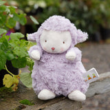 Purple plush lamb toy with a white tag on a wooden surface with plants in the background