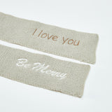Two beige knitted scarves with embroidered text on a white background