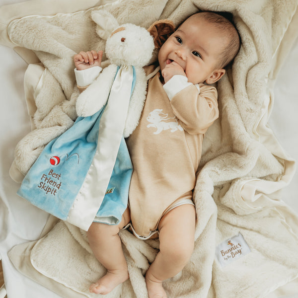 Baby lying on a blanket with a plush toy, surrounded by soft textures