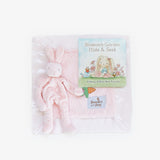 Pink bunny plush toy and book titled 'Blossom's Garden Hide & Seek' with a pink blankie on a white background.