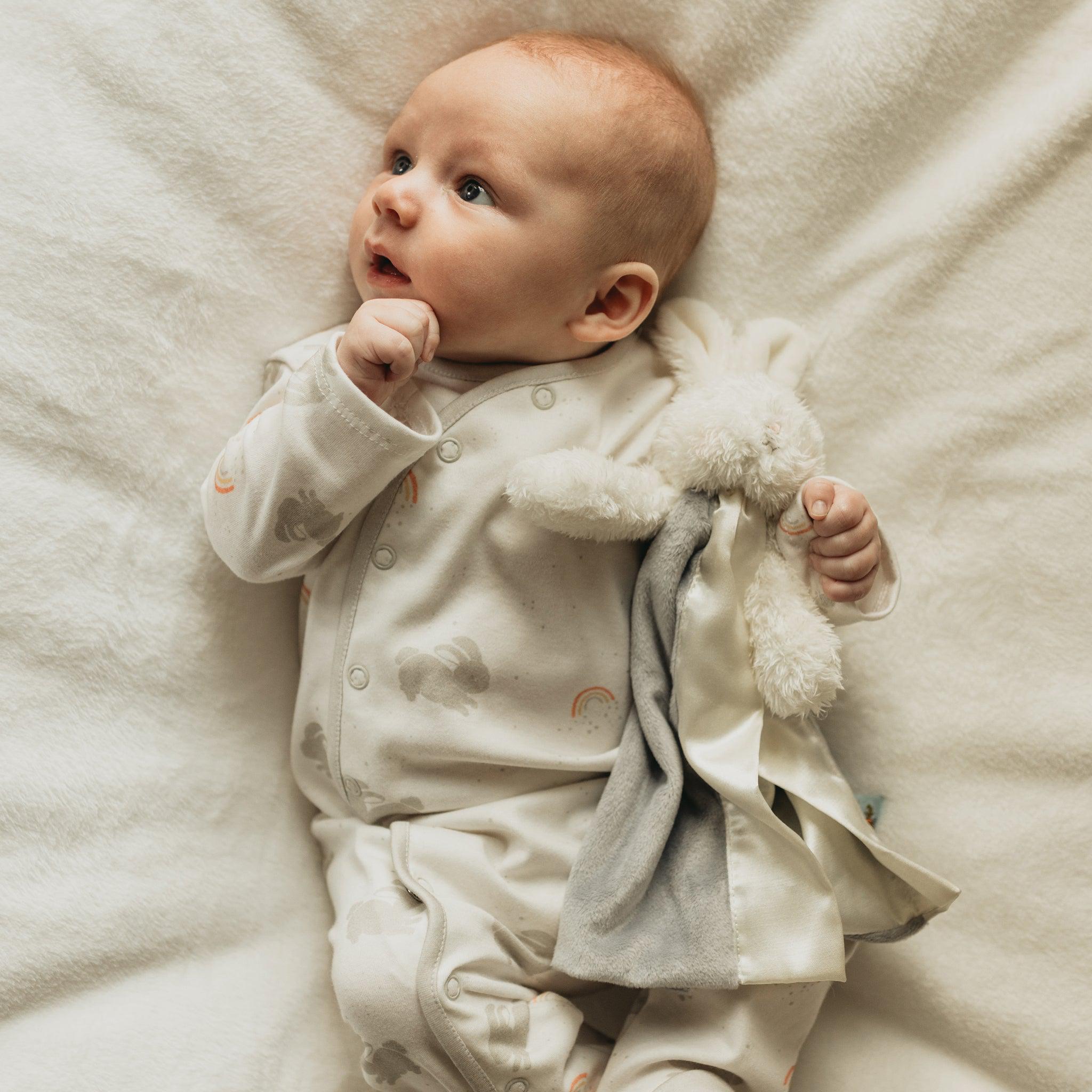 Baby holding a plush bunny lovey on a soft white background